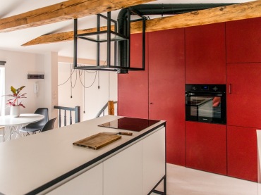 Zabudowa w kuchni ma czerwony kolor i jest całkowicie gładka. Wbudowany piekarnik i zamknięte szafki tworzą prostą konstrukcję, która podkreśla nowoczesny charakter...