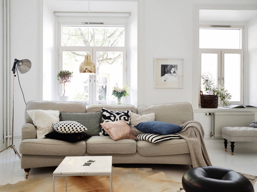Jasno-beżowa sofa na kólkach,kwadratowy stolik kawowy,miedziana lampa wiszaca i dywan z bydlęcej skóry w salonie