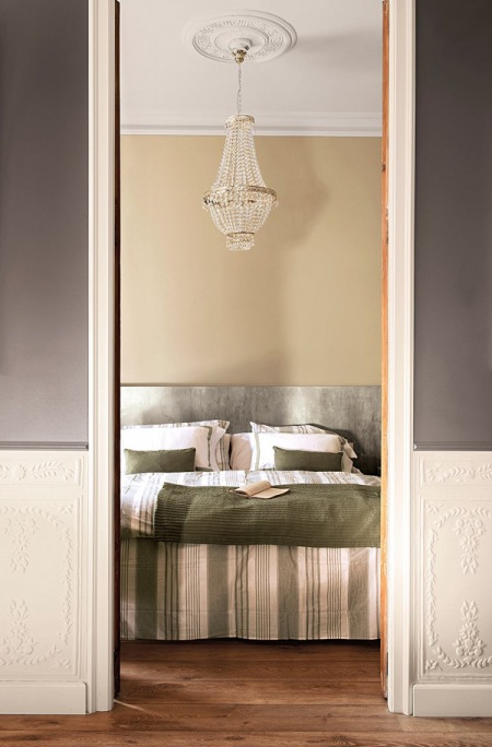 Szaro-beżowe ściany , kryształowy żyrandol i prosta dekoracja łóżka w sypialni