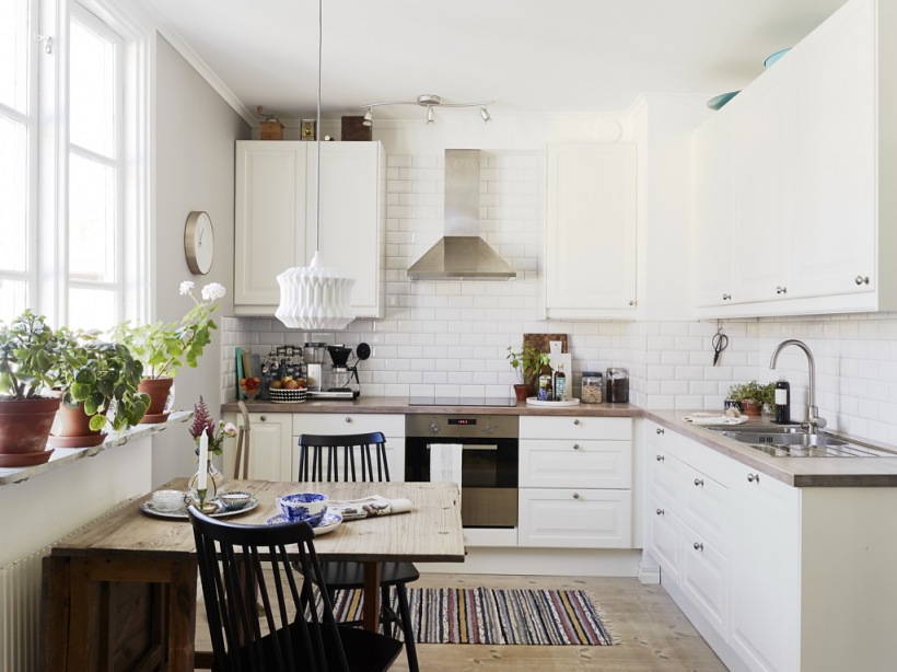 Biała kuchnia w stylu skandynawskim,drewniany rozkładany stół,tkany dywanik na podłodze z drewnianych desek