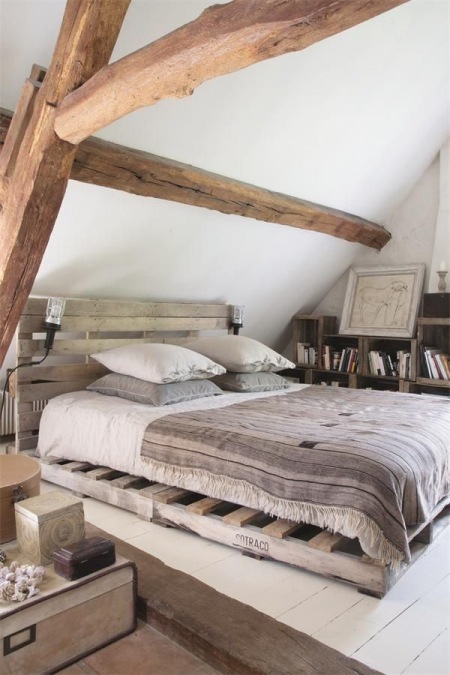 Łóżko z palety , regały z pólkami z drewnianych skrzynek w rustykalnej sypialni na poddaszu z belakami