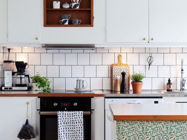 Białe szafki i drewniane deski na podłodze w kuchni wpisują się w styl skandynawski aranżacji. Podkreślają jego...