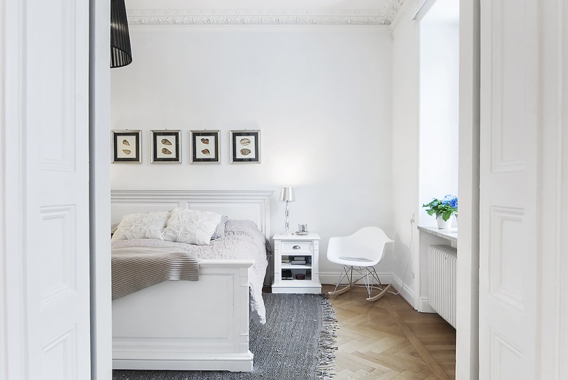 Białe łóżko z drewna,artprinty na ścianie i szary tkany dywan w skandynawskiej  sypialni