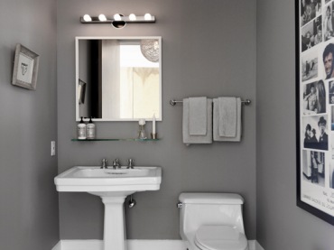 Niewielka, ale bardzo przyjemna łazienka urządzona w nowoczesnym stylu z dominującym kolorem ciemnej szarości oraz piękną drewnianą podłogą. Ciekawe dekoracje, jak chociażby duża rama ze zdjęciami wprowadzają do wnętrza 
