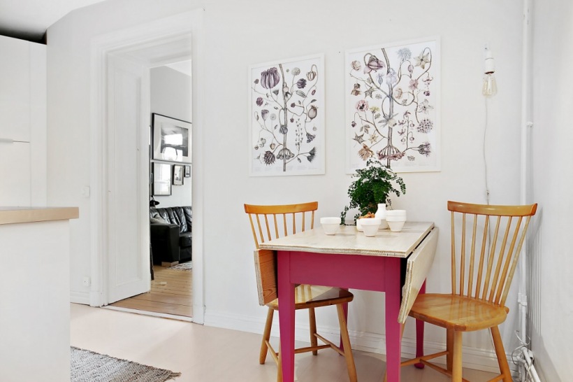 Botaniczne plakaty, różowy stół z drewnianym blatem i żarówka na kablu w dekoracji kuchni
