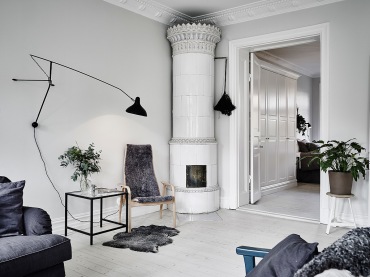 Biały ceramiczny piec w klasyczneym skandynawskim stylu,czarny kinkiet na wysięgniku,bielone deski z drewna na podłodze w salonie (47751)