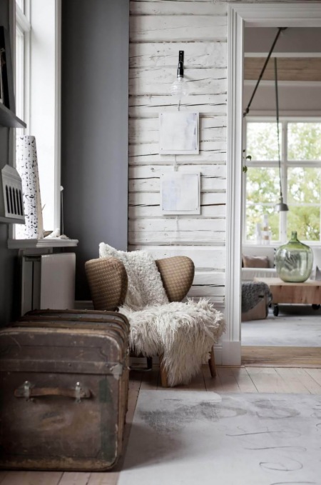 Brązowy fotel uszak,szare ściany,białe bielone drewno na scianie,brązowy retro kufer w stylu vintage i biały drukowany dywan