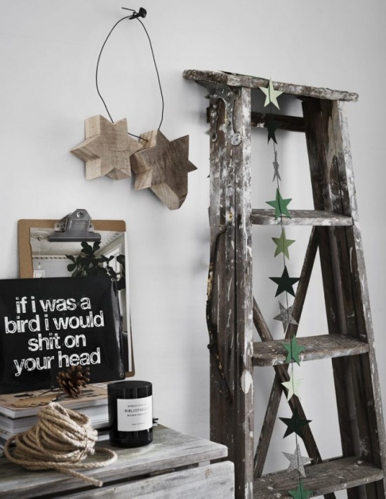 Drewniana drabina ze świątecznymi gwiazdkami z kartonu,drewniane gwiazdy wiszące na metalowym drucie na ścianie ,bielony stół z drewna