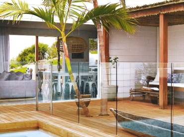 Szklana balustrada wokół basenu,drewniane deski na tarasie z rustykalnym dachem pośród egzotycznych palm (25141)