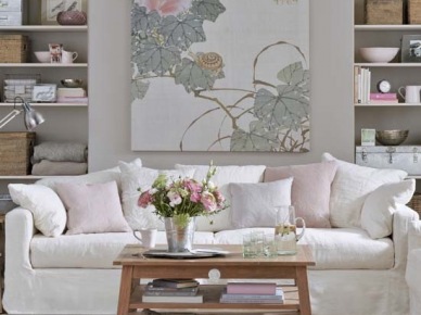 Drewniany tradycyjny stolik kawowy,szaro-różowy obraz z motywem roślin nym,jasnoszare ściany w wbudowanymi białymi pólkami i biała sofa na tkanym dywanie w salonie (26110)