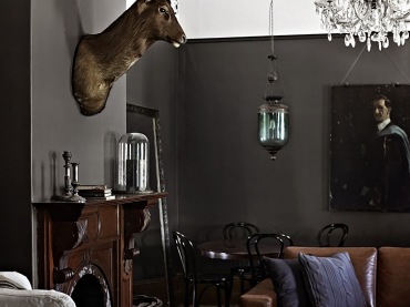 Eklektyczny salon z czarnymi ścianami,stylowym brązowym kominkiem,kryształowym żyrandolem i lampionem z zielonym szkłem (21525)