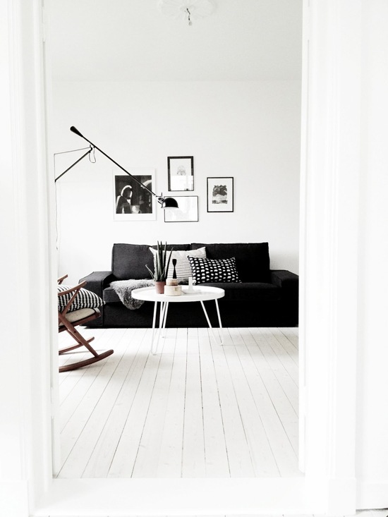 Czarna sofa, czarna lampa podłogowa i czarne ramki z grafikami w białym salonie