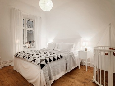 Biało-szaro-czarne trójkaty na skandynawskiej narzucie w białej sypialni małżeńskiej z drewnianym dziecięcym łóżeczkiem (27100)