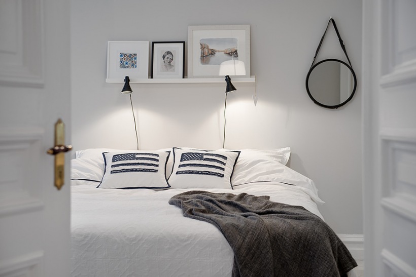 Skandynawska biała sypialnia z czarnymi kinkietami i okrągłym lustrem na ścianie