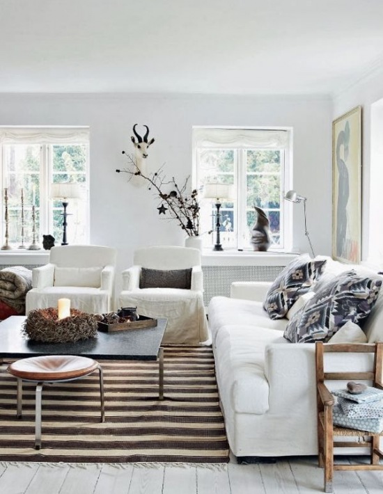 Białe sofy w salonie,drewniane fotele,biało-brązowy dywan w pasy i małe stoliki kawowe i monochromatyczne kolory poduszek dekoracyjnych