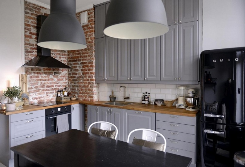 Czarny okap i lampy pendant w aranzacji szarej kuchni ze ścianą z czerwonej cegły