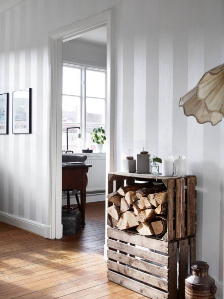 Podłoga z desek,drewniane skrzynki z drewnem i szaro-biała tapeta w pasy szerokie na ścianie