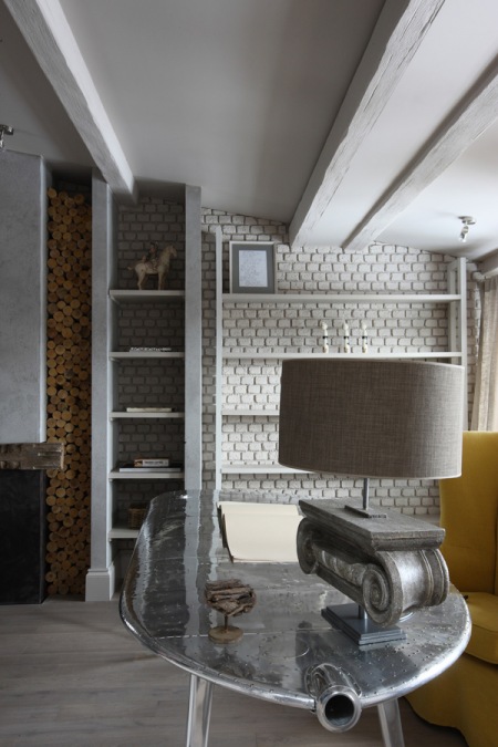 Ściana z białej cegły z półkami,wnęką na drewno kominkowe, francuska lampa vintage i industrialny stolik