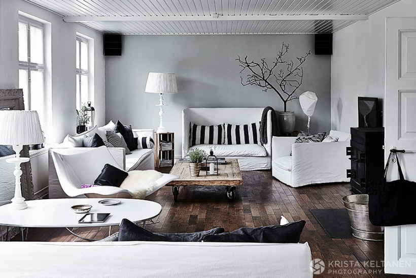 Szara ściana,ciemnobrązowa podłoga,białe meble w lnianych białych ubrankach,czarne detale dekoracyjne w salonie