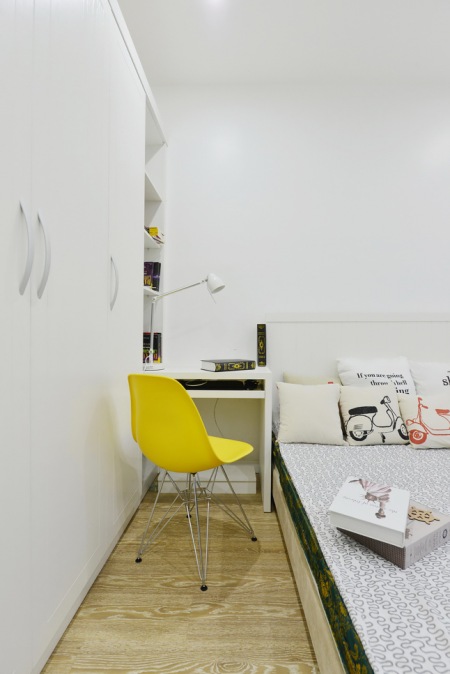 Biała zabudowa szaf i żółte krzesło na metalowych krzyżakach w aranżacji nowoczesnej sypialni