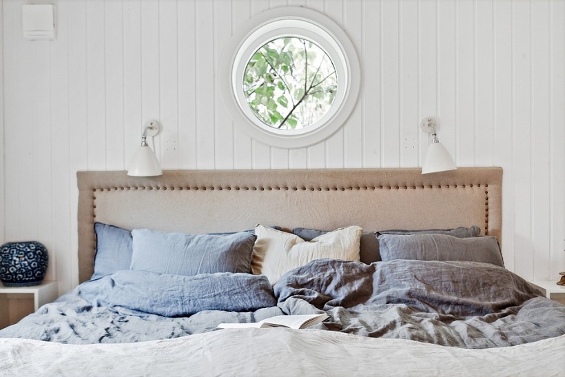 Sypialnia z okrągłym oknem i łóżkiem w beżowej tapicerce