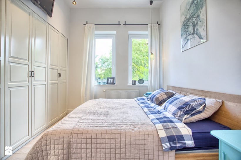 Mała sypialnia z dużym łóżkiem i białą szafą wnękową na całą szerokość ściany