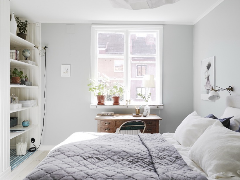 Szaro-liliowa narzuta pikowana na łóżku w sypialni z wnęką ścienną z półkami,drewniane biurko pod oknem