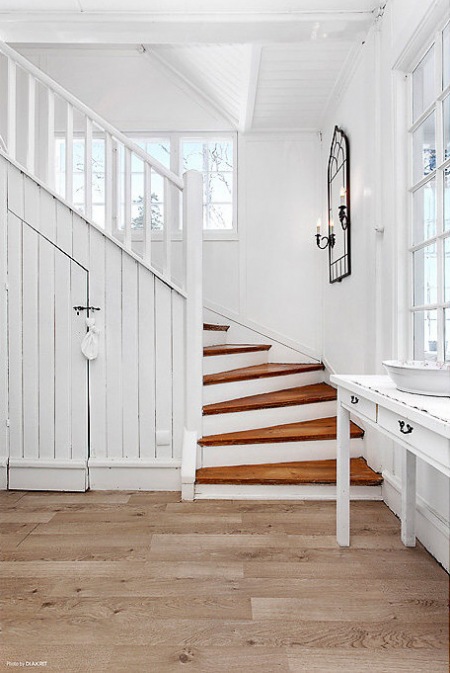 Biała konsolka z lustrem przy    drewnianych  schodach w domu