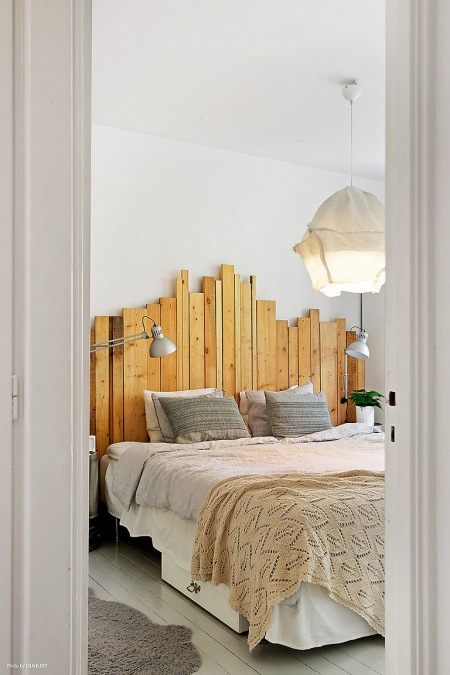 Drewniane wezgłowie z surowych desek i lampa z drutu i bawelny nad łóżkiem w sypialni