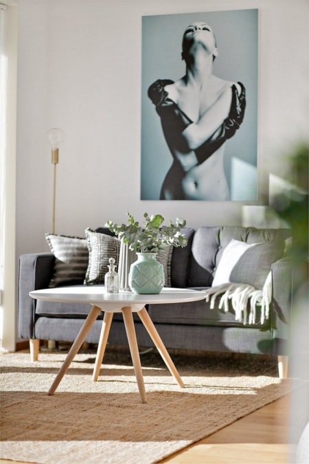 Duże fotografie na ścianie nad grafitową sofą,miętowe dodatki w aranżacji białego salonu z okragłym nowoczesnym stolikiem