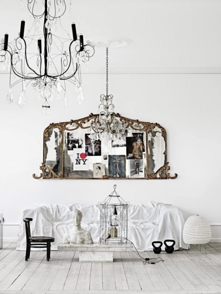 Francuskie rzeźbione ramki z fotografiami jako ozdoba na ścianie nad biała sofą i kutymi żyrandolami z kryształkami