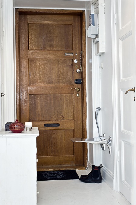 Składane krzesełko i drewniane drzwi wejściowe w białej aranżacji wnętrza
