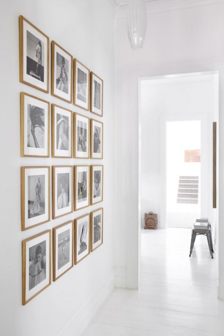 Galeria czarno-białej fotografi w drewnianych ramkach na białej ścianie w przedpokoju