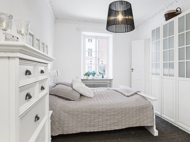 Biała komoda z szufladami,nowoczesna czarna lampa,szafa z witrynami i szara narzuta na łóżku w skandynawskiej sypialni (21987)