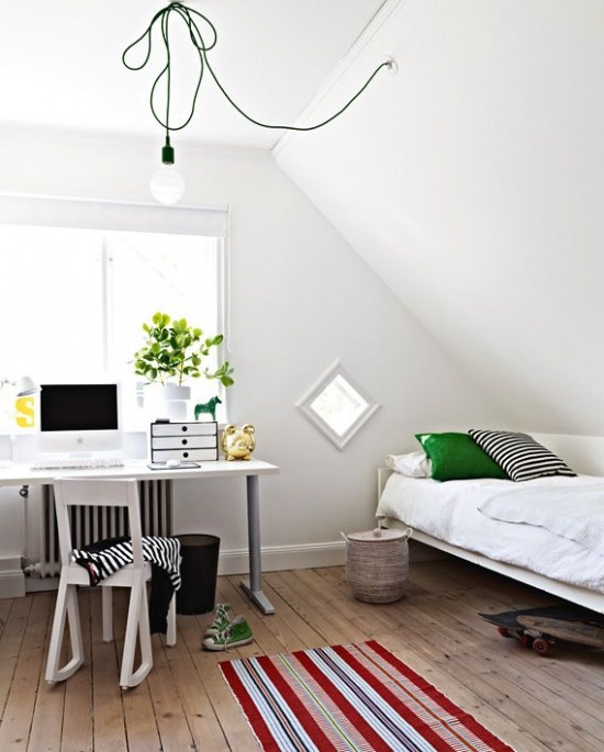 Żarówka na kablu,podłoga z drewnianych desek i metalowe łóżko z biurkiem
