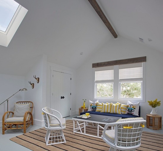 Białe meble z rattanu, beżowy dywan i żółto-niebieskie poduszki w aranżacji pokoju