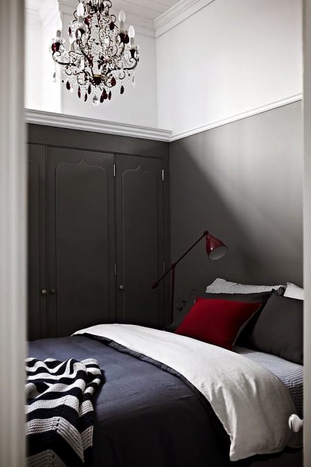Żyrandol z kryształkami w szarej sypialni z czerwoną lampką i poduszką na łóżku