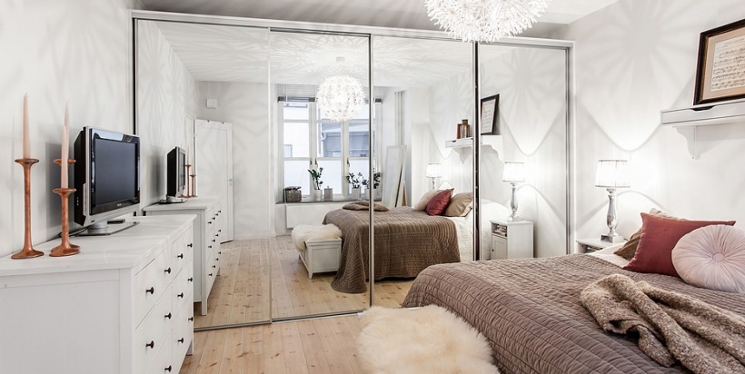 Biała sypialnia z lustrzaną szafą, białą komodą i beżowo-różową dekoracją łóżka