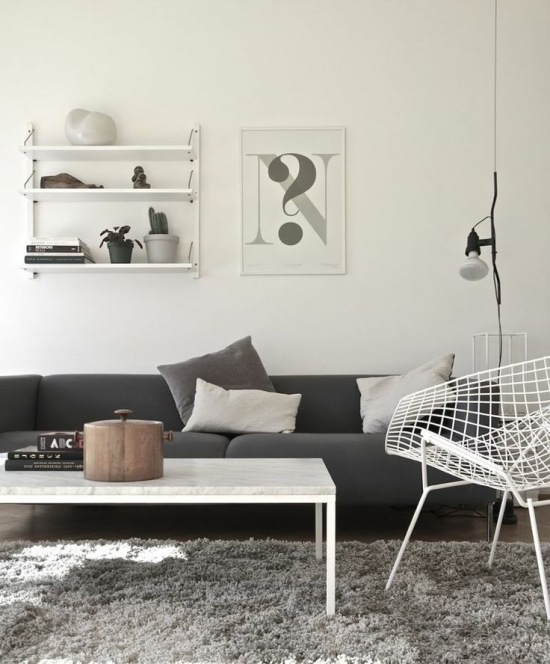 Szara nowoczesna sofa,biały stolik,biały metalowy fotel z azurami i grafiki z pólkami na ścianach