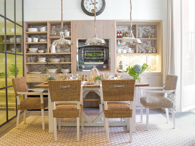 Biały tradycyjny stół z drewnianym blatem,drewniane krzesła z plecionymi siedziskami i oparciami,chromoniklowane rustykalne lampy wiszące,otwarte półki i przeszklona ściana w dużej kuchni