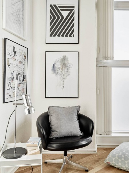 Nowoczesne biało-czarne grafiki,czarny skórzany fotel ,srebrna lampa biurkowa i biały stolik z tacą