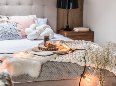 W sypialni na poddaszu wiele elementów wpływa na jej klimat. Wystarczy spojrzeć na drewniane ściany i szafki nocne, ciepłe poduszki i pledy, nastrojową girlandę...