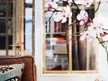 Pina brazowa sofa w pokoju dziennym w otoczeniu poduch i kwiatow