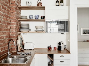 Biała kuchnia skandynawska z drewnianymi blatami i półkami i ścianą z czerwonej cegły (27035)