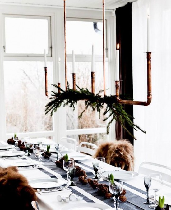 Wiszący świecznik z miedzianych rurek z gałązka igliwia nad świątecznym stołem w stylu skandynawskim