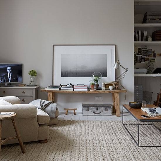 Tkany dywan,industrialny stolik,drewniana ławka z grafiką w ramach i wnęka z pólkami w salonie skandynawskim
