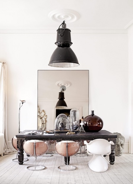 Olbrzymia czarna lampa pendant,prostokątna tafla lustra przy ścianie w jadalni z desingerskimi krzesłami muszlami,stylowym lakierowanym stołem,brązowy wazon pękaty,szklane dekoracje
