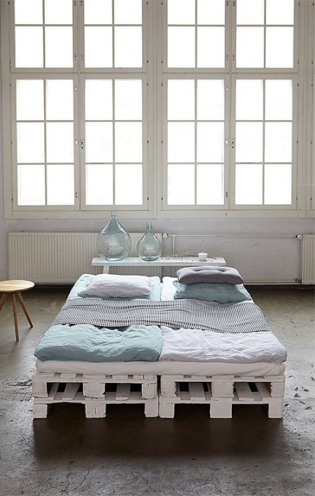 Pomalowane na biało palety w roli  bazy łóżka  w aranżacji  sypialni w industrialnym stylu