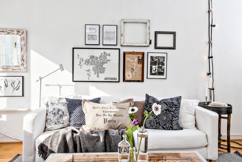 Girlanda z żarówek na czarnym kablu,skandynawskie grafiki na ścianie nad białą sofą z dekoracyjnymi poduszkami