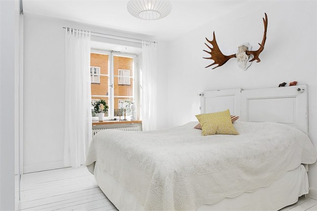 Białe łóżko vintage , poroże jelenia w aranżacji białej sypialni